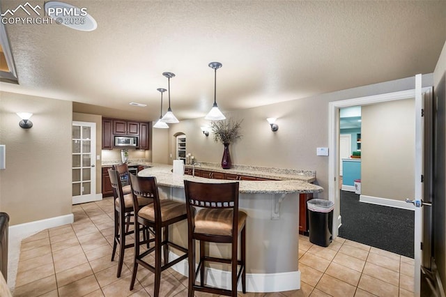 kitchen featuring stainless steel microwave, a kitchen breakfast bar, hanging light fixtures, light tile patterned floors, and kitchen peninsula