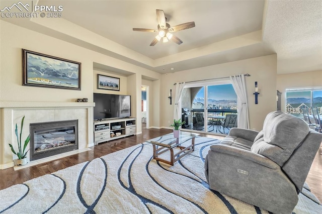 living room featuring a tiled fireplace, a tray ceiling, plenty of natural light, and hardwood / wood-style flooring