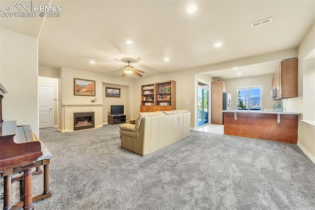 carpeted living room with a tiled fireplace and ceiling fan