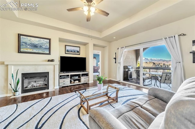 living room featuring a raised ceiling, hardwood / wood-style flooring, ceiling fan, and a tile fireplace