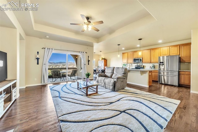 living room with dark hardwood / wood-style floors, ceiling fan, and a raised ceiling