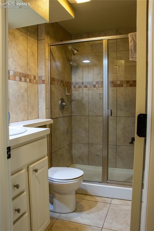 bathroom featuring vanity, toilet, a shower with shower door, and tile patterned flooring