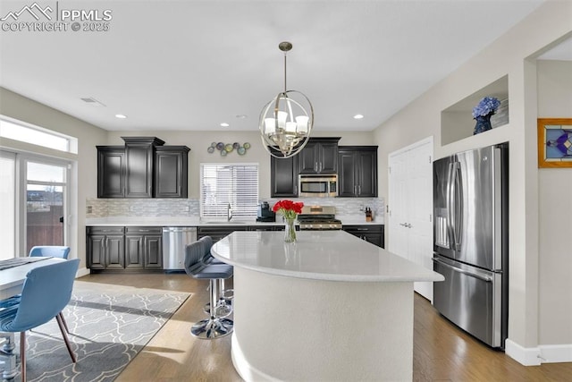 kitchen with light countertops, appliances with stainless steel finishes, pendant lighting, light wood-type flooring, and a center island