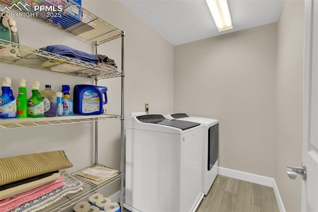 clothes washing area featuring laundry area, light wood-style flooring, baseboards, and washing machine and clothes dryer