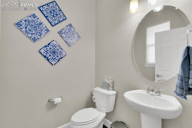 half bathroom with a sink, baseboards, and toilet