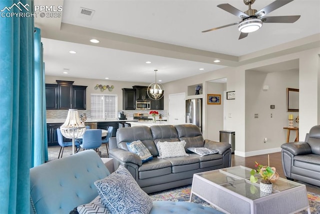 living area with visible vents, baseboards, recessed lighting, light wood-style floors, and ceiling fan with notable chandelier