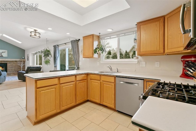 kitchen featuring a brick fireplace, open floor plan, appliances with stainless steel finishes, a peninsula, and a sink