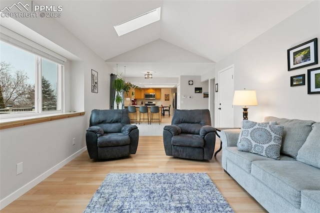 living area featuring vaulted ceiling with skylight, wood finished floors, and baseboards