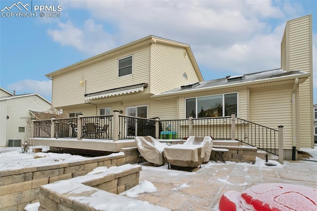 snow covered property with cooling unit, a chimney, and a deck