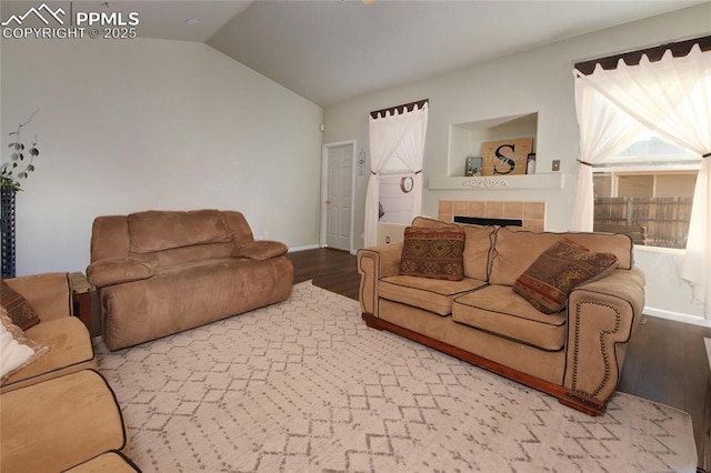 living room featuring lofted ceiling, wood finished floors, baseboards, and a tile fireplace