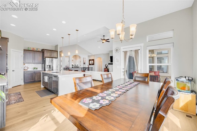 dining space featuring sink, ceiling fan with notable chandelier, vaulted ceiling, and light wood-type flooring