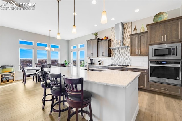 kitchen featuring appliances with stainless steel finishes, pendant lighting, sink, light stone counters, and wall chimney exhaust hood