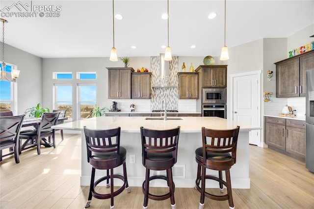 kitchen with wall chimney range hood, appliances with stainless steel finishes, hanging light fixtures, a kitchen breakfast bar, and a spacious island