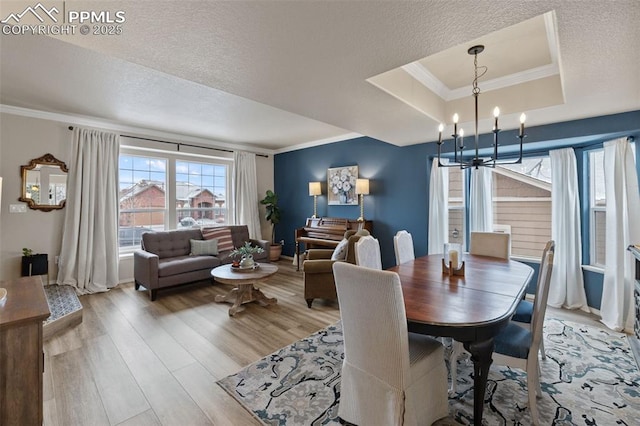 dining room featuring hardwood / wood-style floors, a chandelier, ornamental molding, a raised ceiling, and a textured ceiling