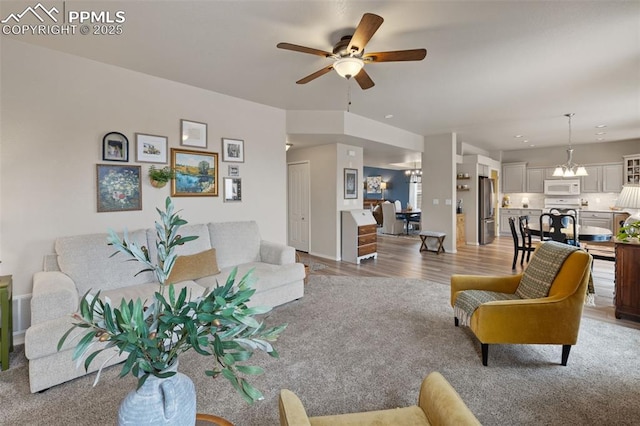 living room featuring ceiling fan with notable chandelier and light hardwood / wood-style flooring