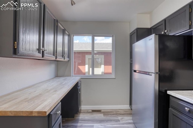 kitchen with gray cabinets, butcher block countertops, and stainless steel refrigerator