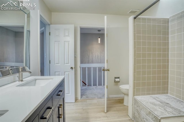 bathroom with hardwood / wood-style flooring, tiled shower, vanity, and toilet