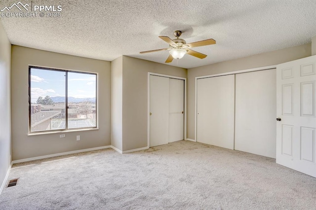 unfurnished bedroom featuring ceiling fan, a textured ceiling, light carpet, and two closets