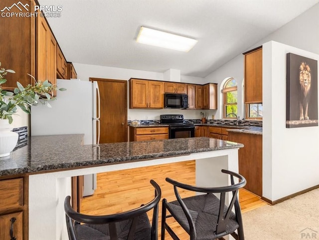 kitchen with a peninsula, black appliances, brown cabinetry, and dark stone countertops