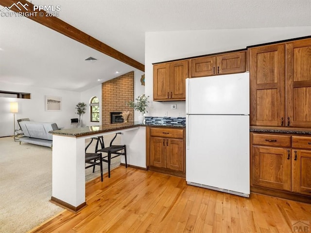 kitchen featuring vaulted ceiling with beams, brown cabinetry, freestanding refrigerator, open floor plan, and a peninsula