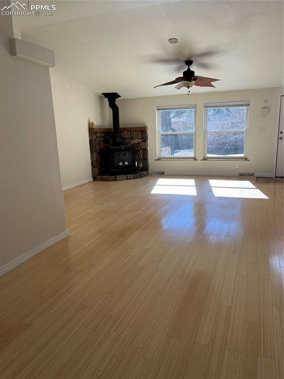 unfurnished living room featuring a wood stove, ceiling fan, and light hardwood / wood-style flooring