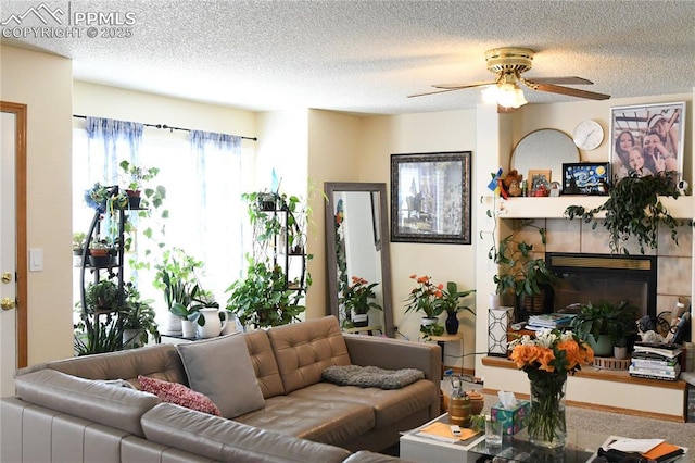 living room featuring ceiling fan, a tile fireplace, and a textured ceiling