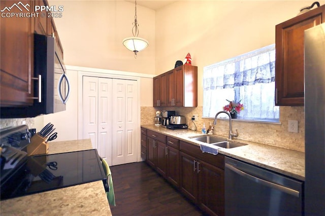 kitchen featuring pendant lighting, a towering ceiling, decorative backsplash, appliances with stainless steel finishes, and a sink