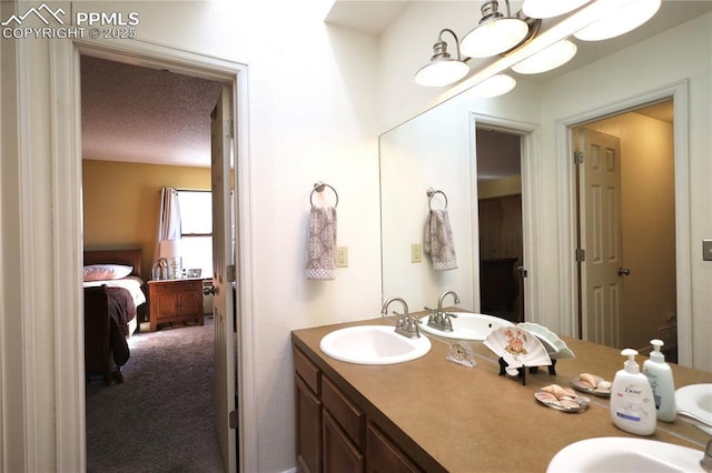 ensuite bathroom featuring a sink, double vanity, a textured ceiling, and ensuite bath