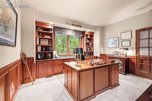 office area with light carpet, visible vents, wainscoting, and built in shelves