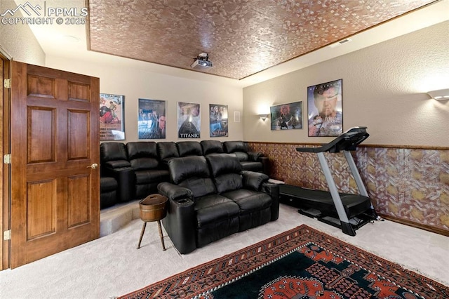 cinema room with a wainscoted wall, visible vents, carpet, a raised ceiling, and a textured wall