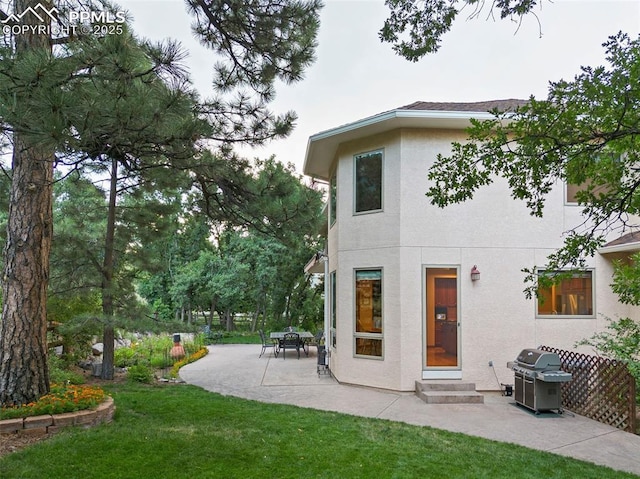 rear view of property featuring stucco siding, entry steps, a lawn, and a patio