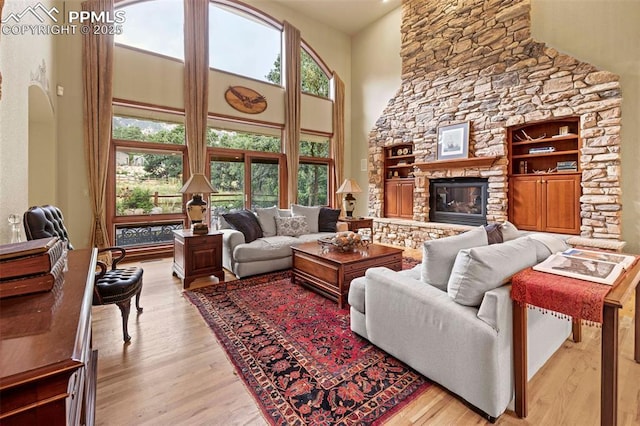 living area featuring a stone fireplace, a high ceiling, and wood finished floors