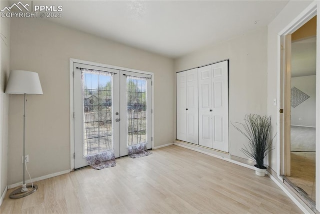 unfurnished bedroom featuring access to outside, baseboards, a closet, french doors, and light wood-style floors