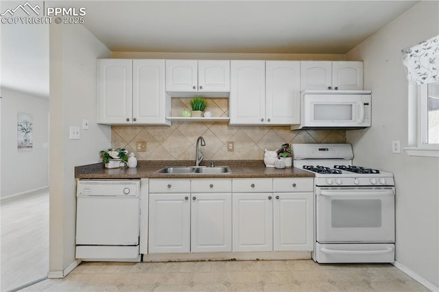 kitchen featuring white appliances, baseboards, a sink, and dark countertops