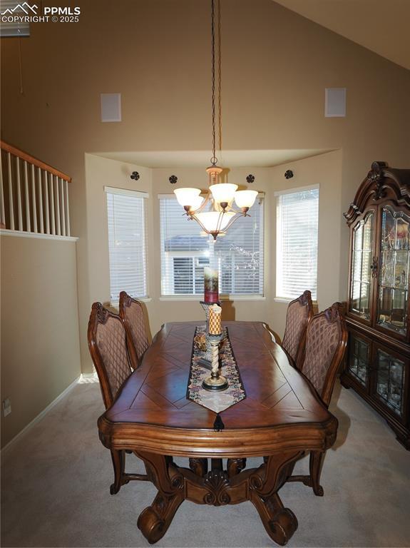 carpeted dining room with a notable chandelier and high vaulted ceiling