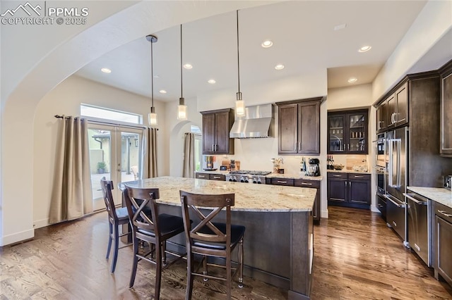 kitchen featuring hanging light fixtures, a kitchen island, dark brown cabinets, and wall chimney range hood