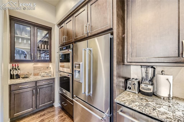 kitchen featuring dark brown cabinetry, light stone counters, and stainless steel appliances