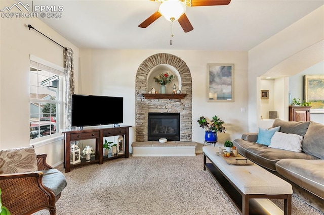 living room with ceiling fan, a stone fireplace, and carpet