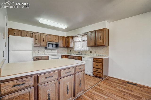 kitchen with tasteful backsplash, sink, white appliances, and light hardwood / wood-style floors