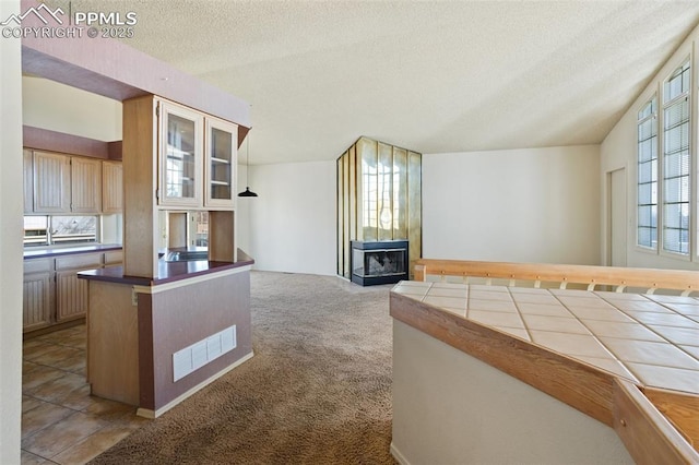 kitchen with tile counters, a fireplace, carpet flooring, and a textured ceiling