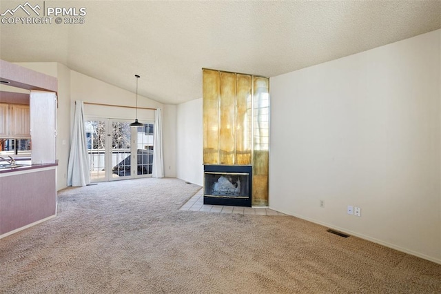 unfurnished living room featuring a tiled fireplace, light colored carpet, a textured ceiling, and lofted ceiling