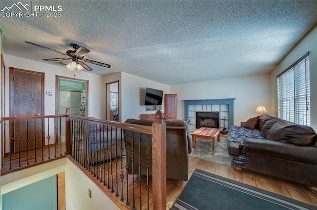 living room with ceiling fan, hardwood / wood-style floors, a tile fireplace, and a textured ceiling