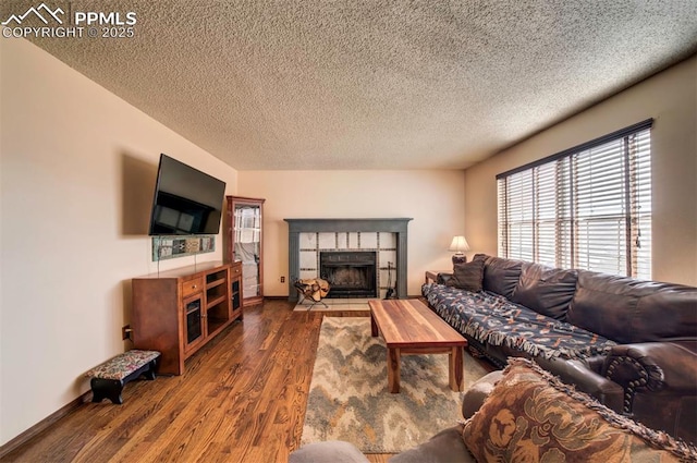 living room featuring a tiled fireplace, dark wood-type flooring, and a textured ceiling