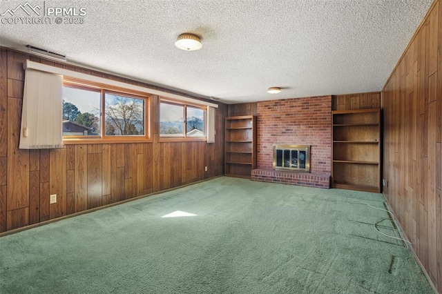 unfurnished living room with a brick fireplace, built in shelves, carpet flooring, wood walls, and a textured ceiling