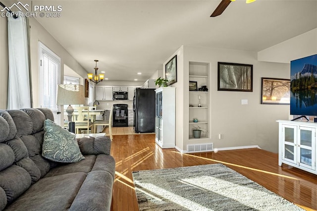 living room featuring built in shelves, ceiling fan with notable chandelier, and hardwood / wood-style flooring