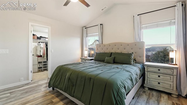 bedroom with a spacious closet, vaulted ceiling, light wood-type flooring, a closet, and ceiling fan