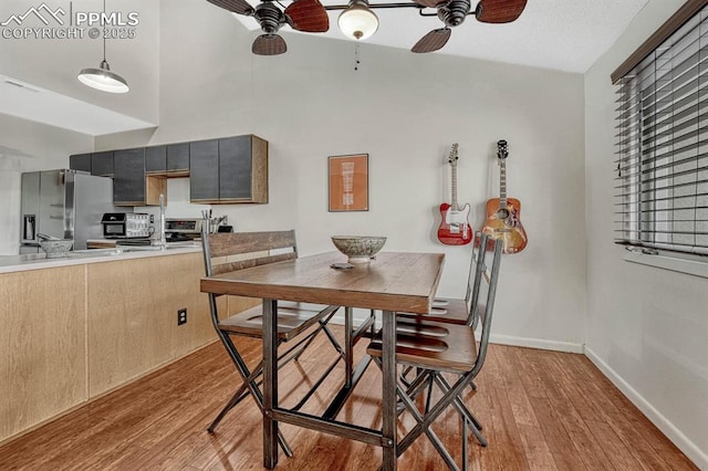 dining space with a towering ceiling, light wood-style floors, baseboards, and a ceiling fan