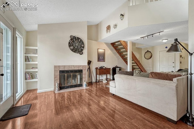 living area with a tiled fireplace, wood finished floors, stairs, a textured ceiling, and a wealth of natural light