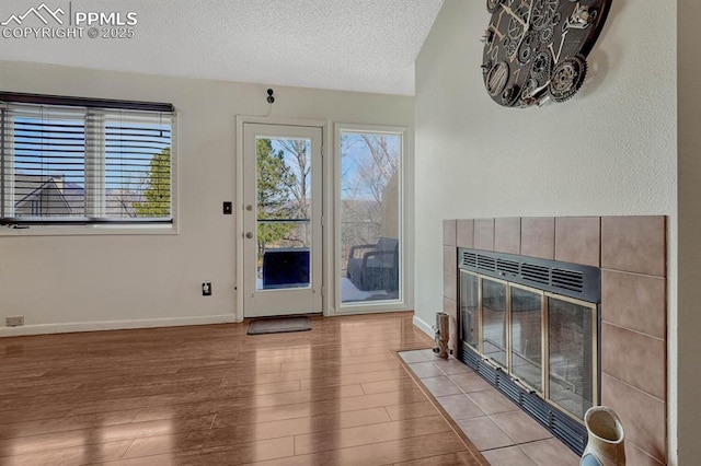 living room featuring a fireplace, a textured ceiling, baseboards, and wood finished floors