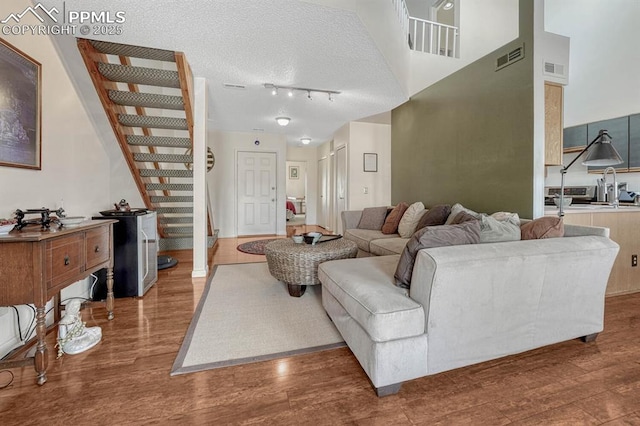 living area featuring a textured ceiling, a high ceiling, wood finished floors, visible vents, and stairs